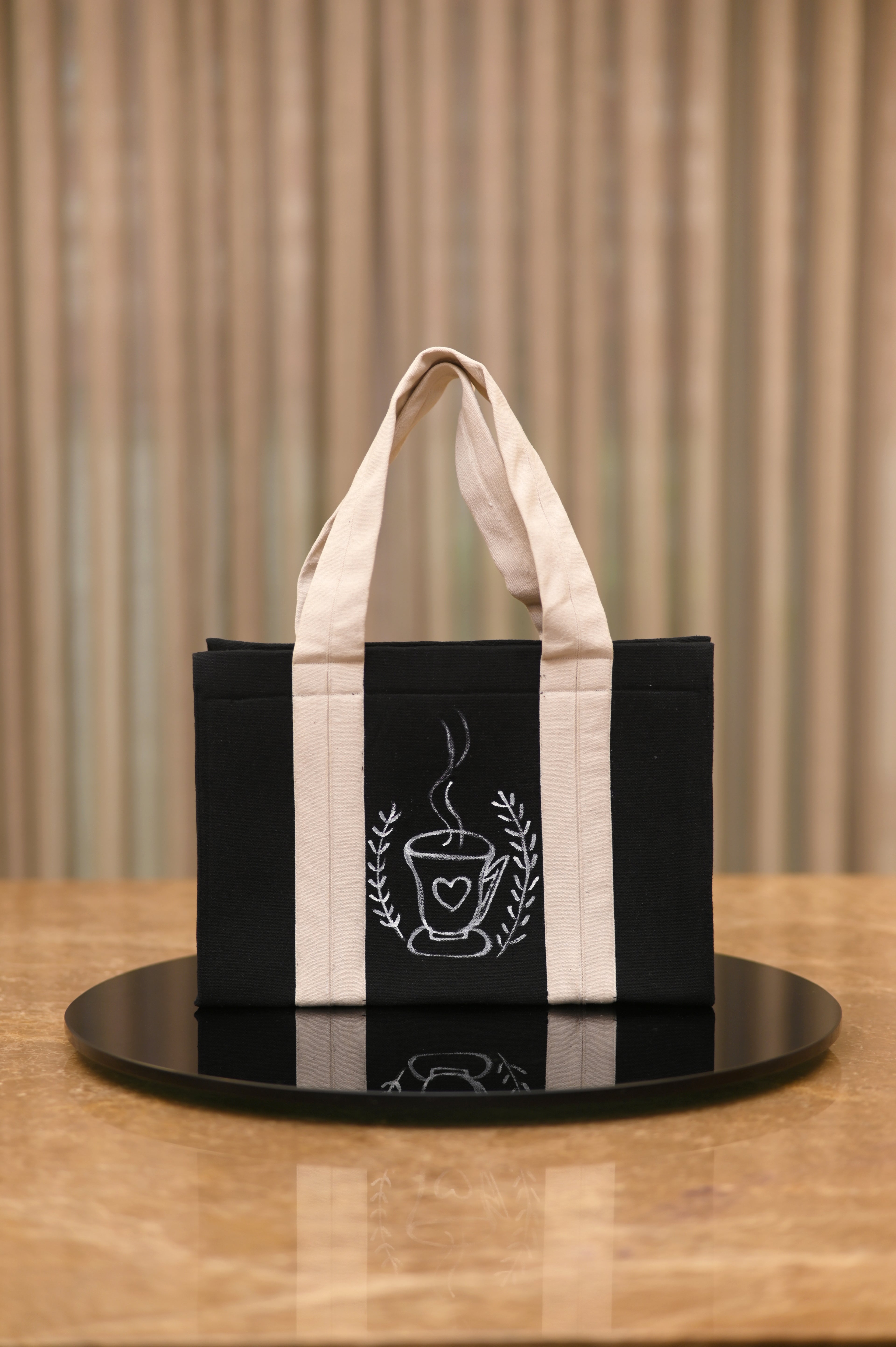 Black and white tote bag with a coffee cup design on a wooden surface.